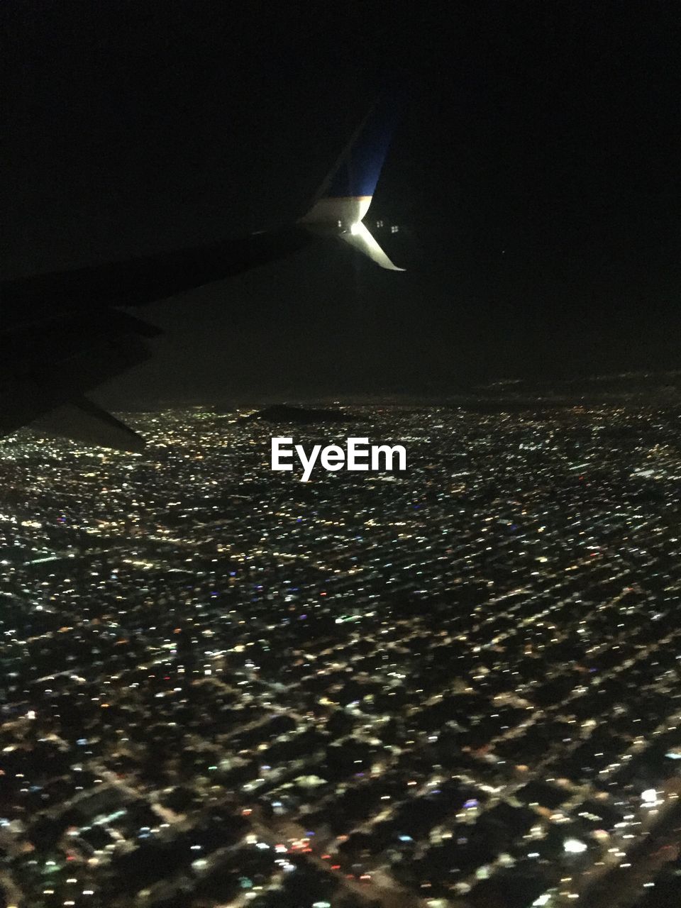 AERIAL VIEW OF ILLUMINATED CITYSCAPE SEEN THROUGH AIRPLANE WINDOW AT NIGHT