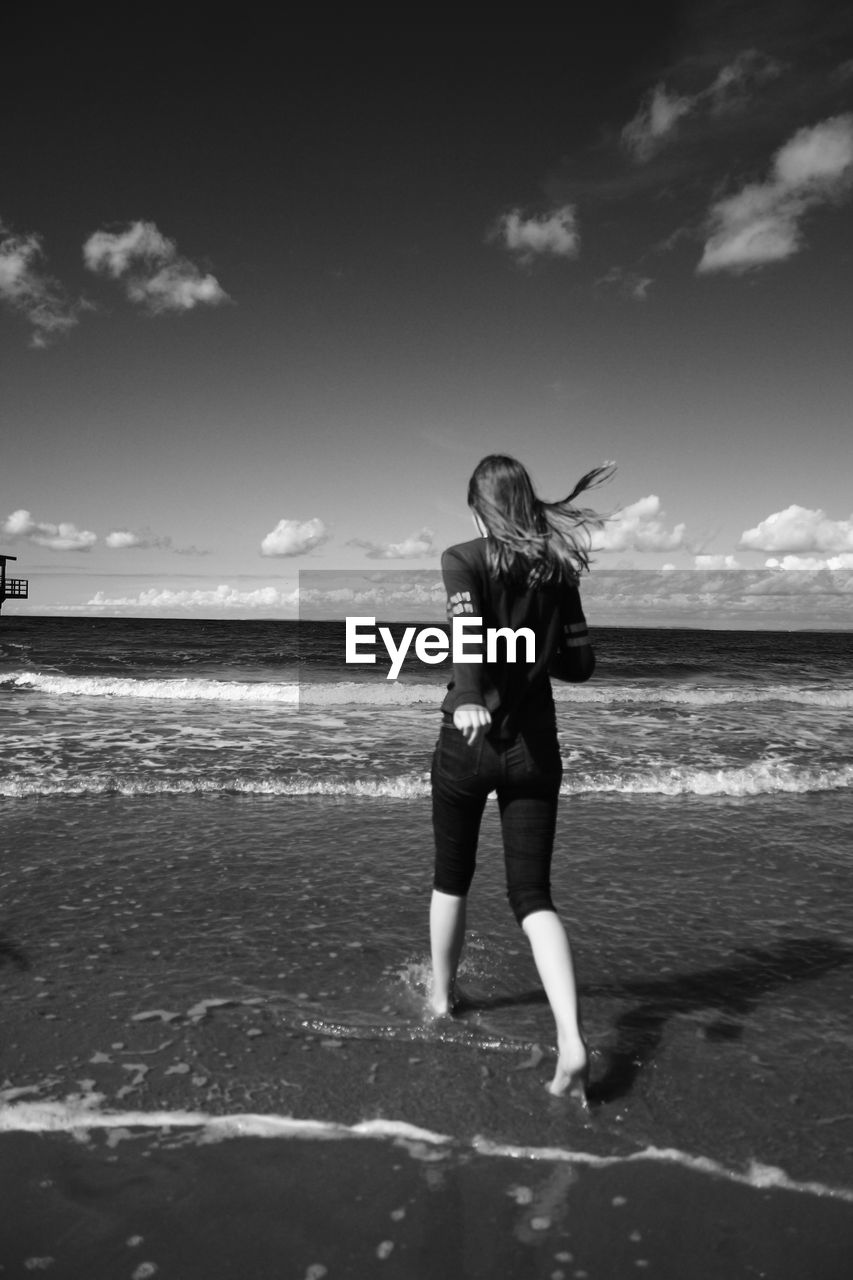 Woman walking on beach against sky