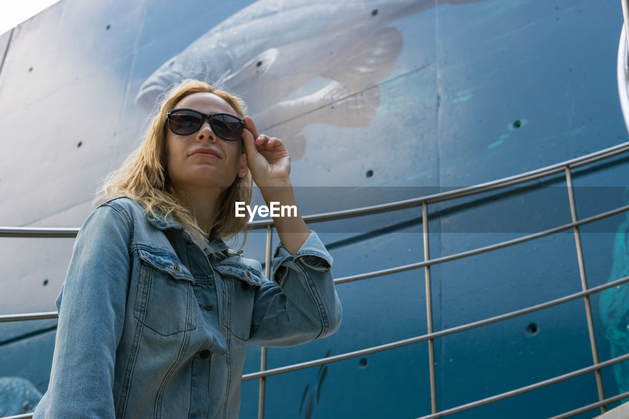 portrait of young woman wearing sunglasses while standing by railing