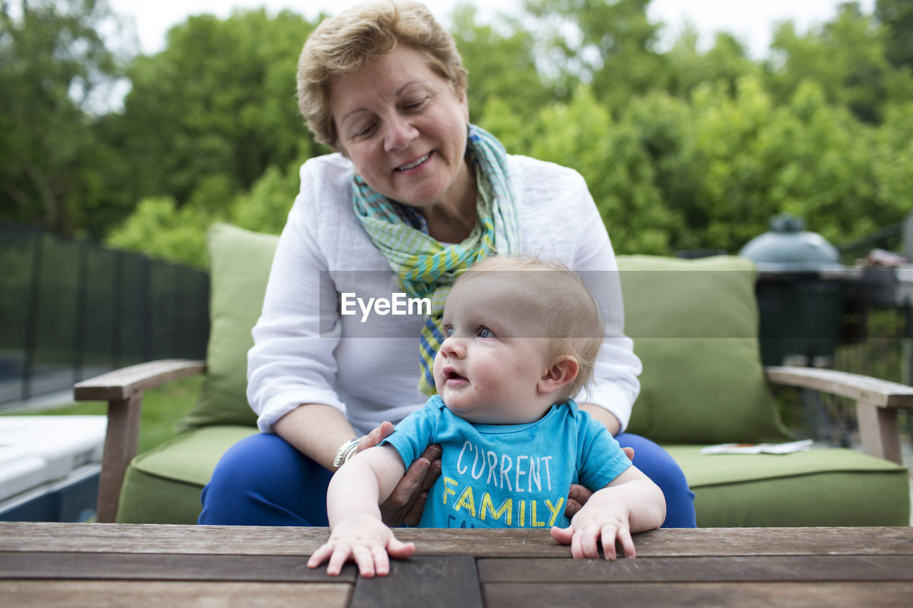 Happy grandma sits on outdoor sofa holding baby grandson