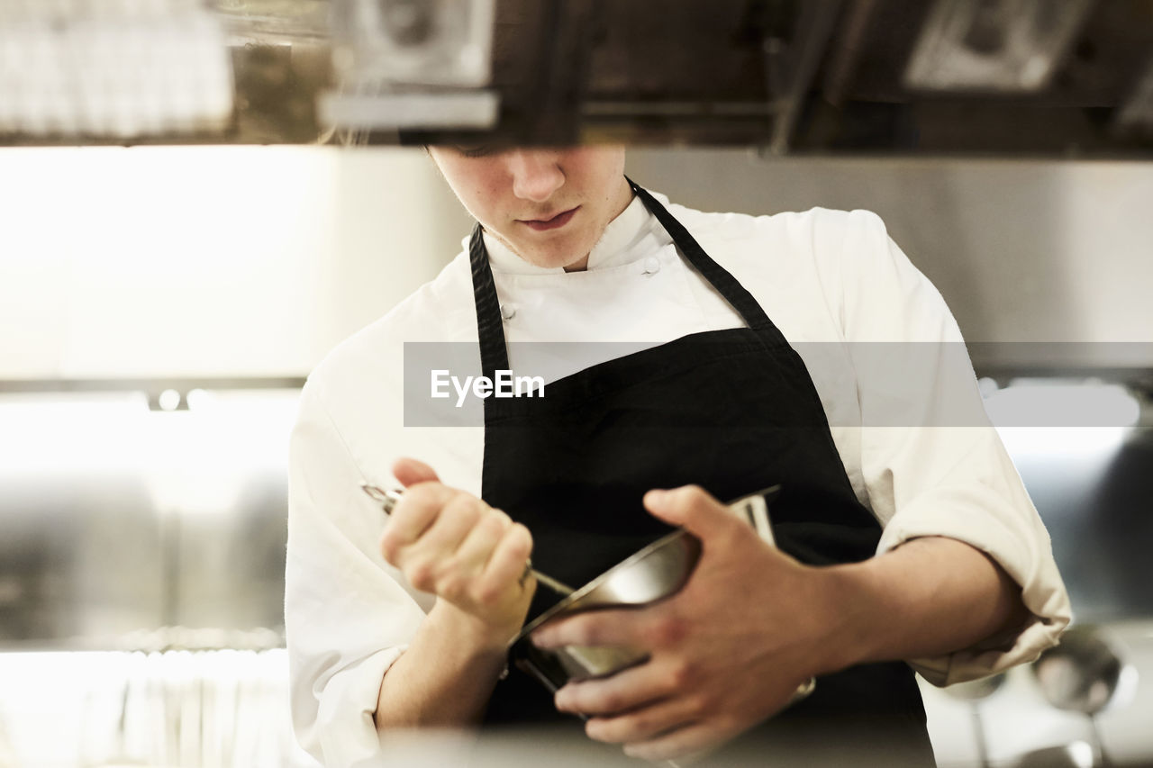 Midsection of male chef mixing food in bowl in commercial kitchen