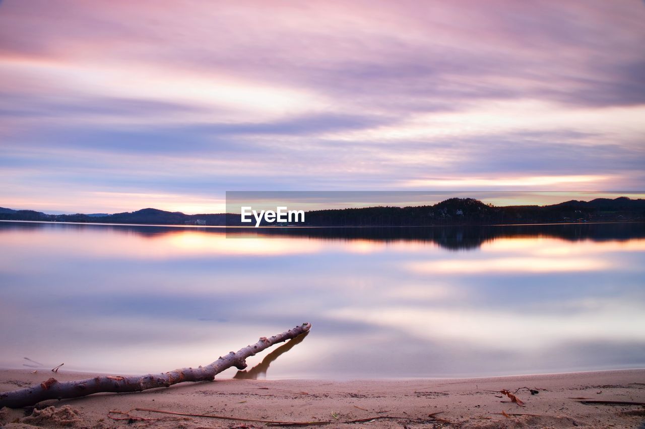 Long exposure landscape of lake shore with dead tree trunk fallen into water
