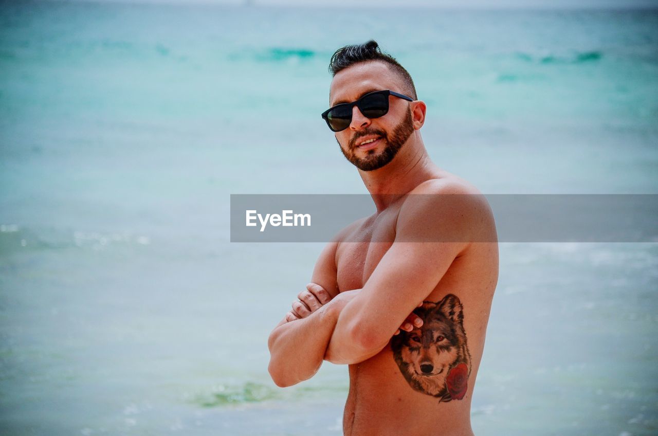 Portrait of shirtless man wearing sunglasses while standing at beach