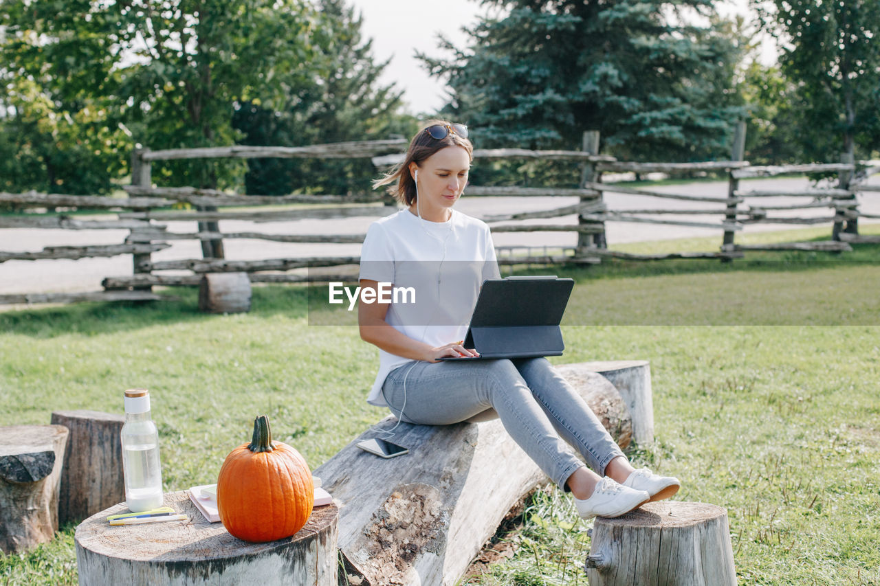 Full length of smiling woman using laptop while sitting at park