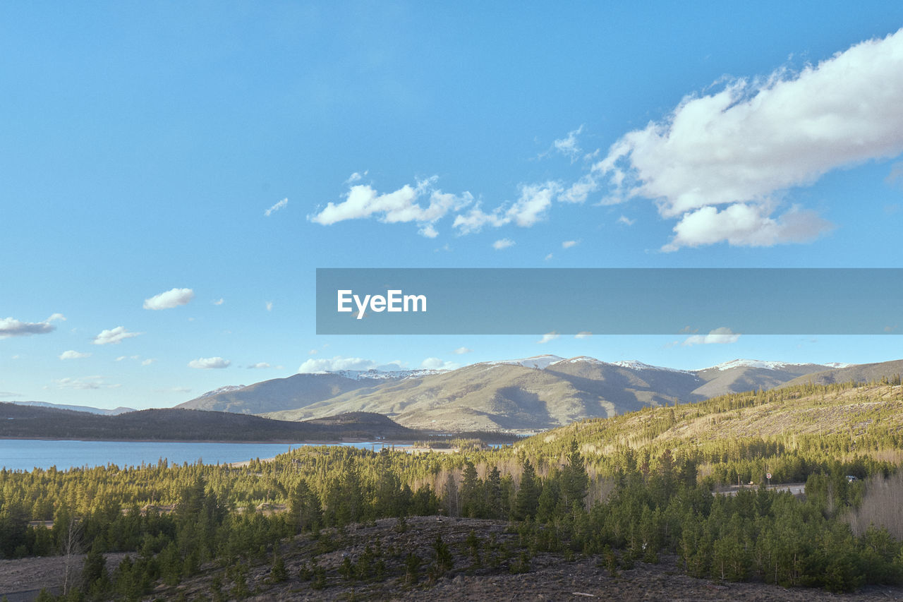 Serene view of mountains, forests, and lake against a clear blue sky