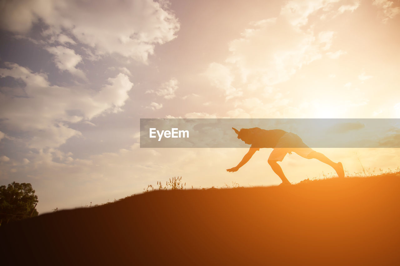 Silhouette man performing stunt on land against sky during sunset