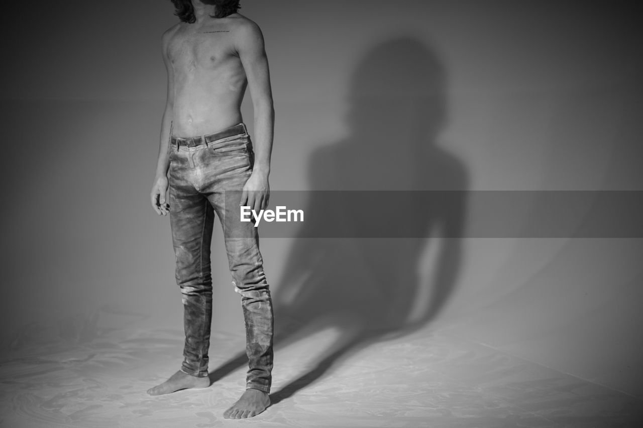 Low section of shirtless man while standing over white background