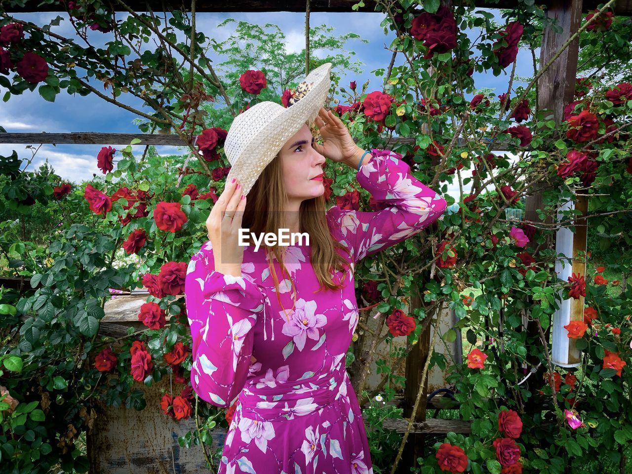 Woman with hat wearing a pink dress in a garden of roses