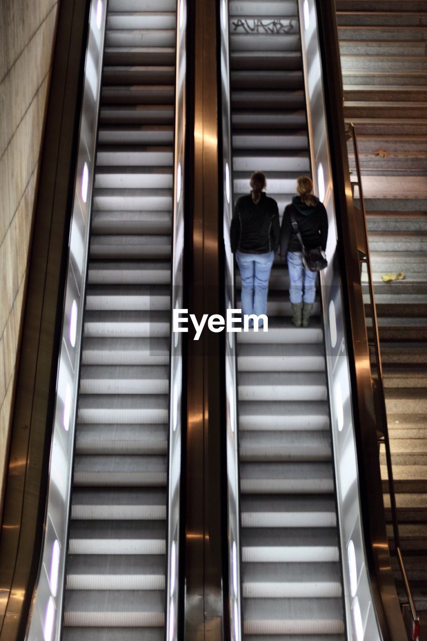 Rear view of two women moving up on escalator