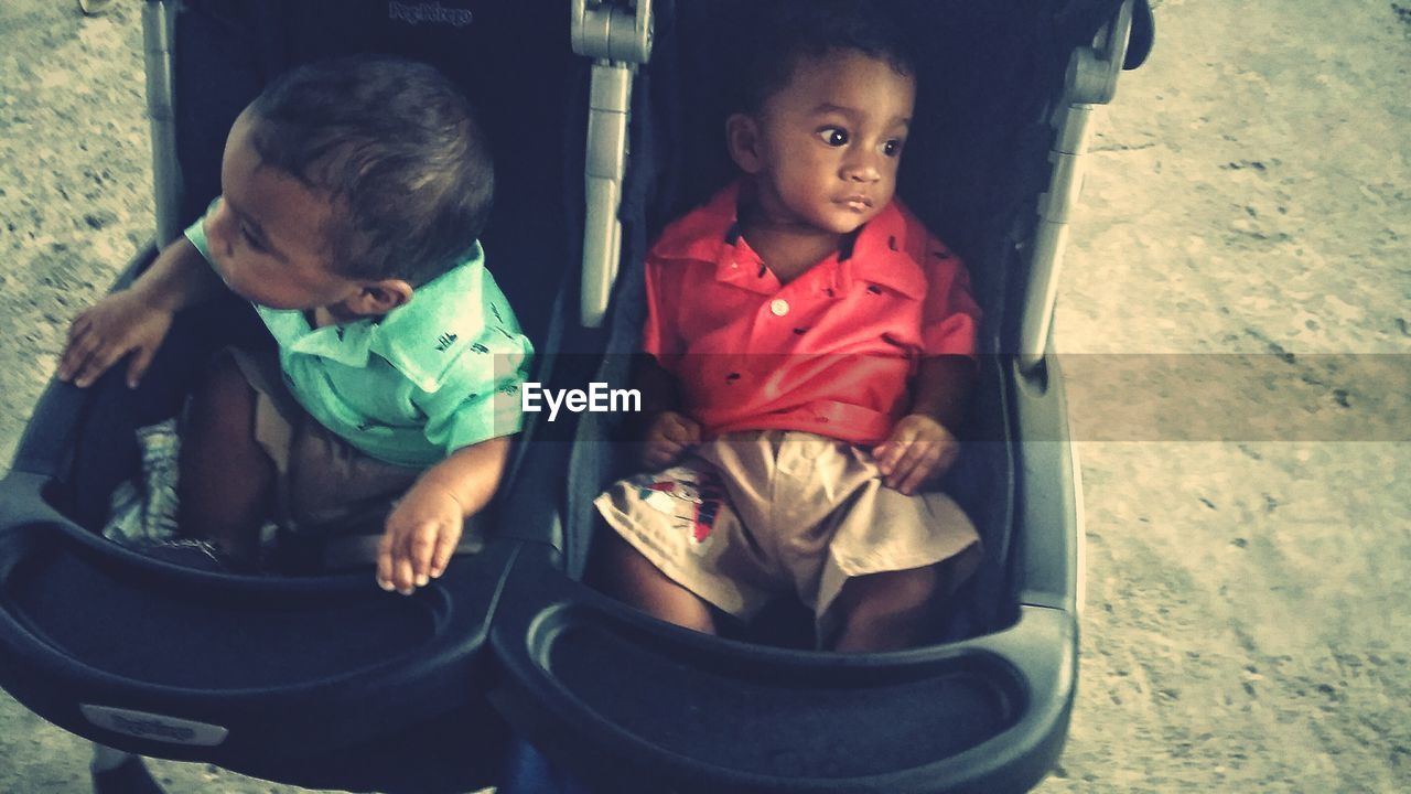 High angle view of cute brothers sitting in baby stroller