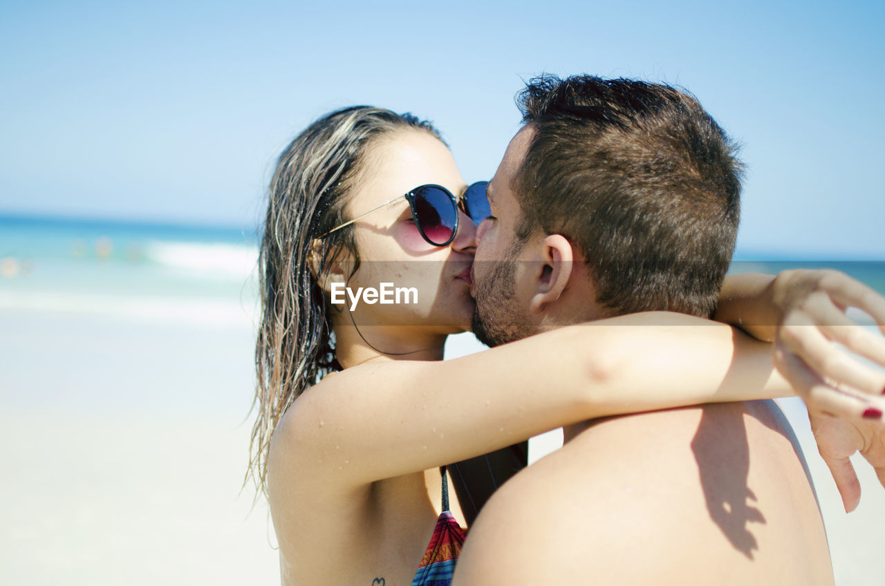 Young couple kissing at beach against clear sky