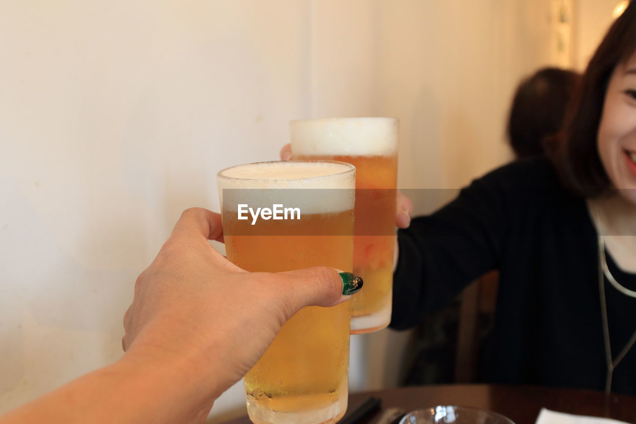 Cropped image of hand toasting beer glass with friend at restaurant