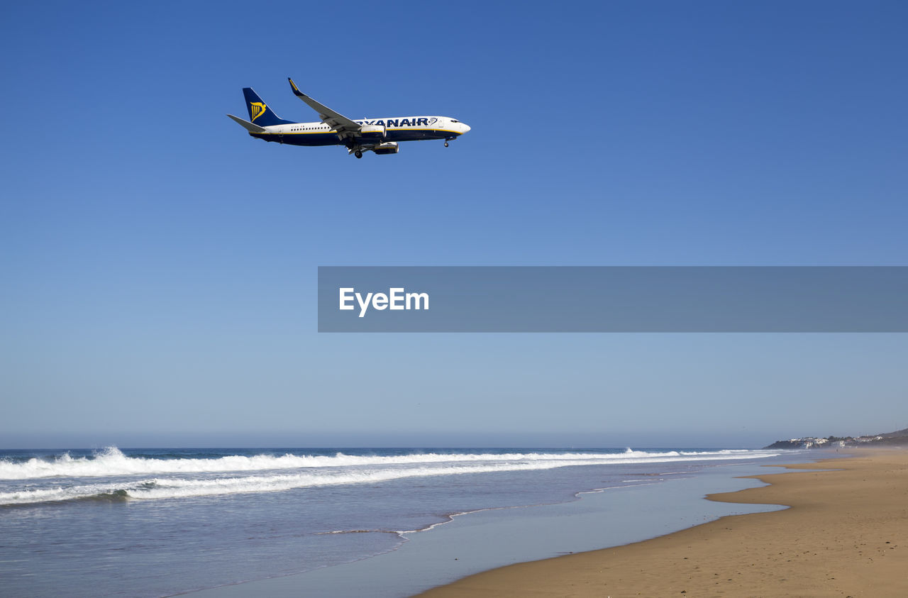 AIRPLANE FLYING OVER BEACH AGAINST CLEAR SKY