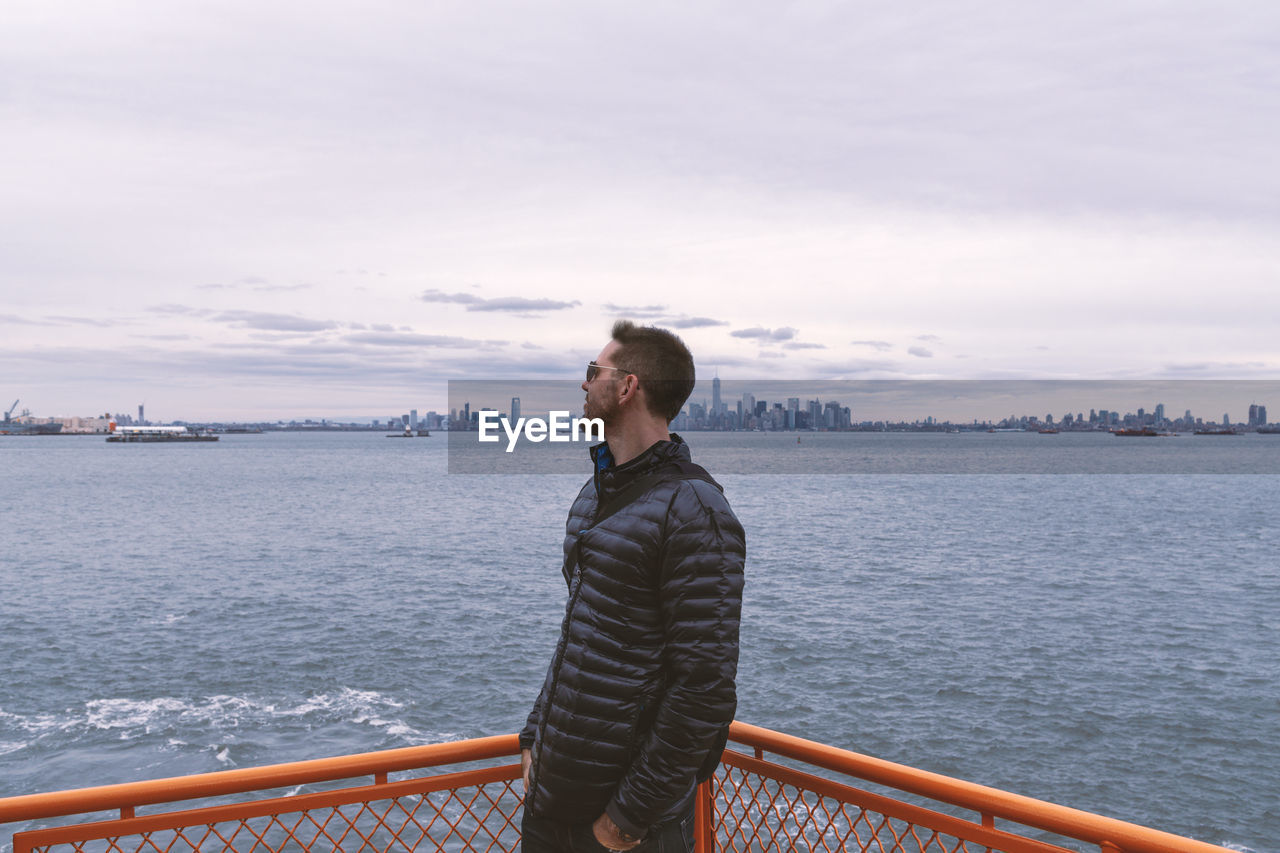 Man riding the staten island ferry gazing  wearing sunglasses and stylish puffer black winter coat.