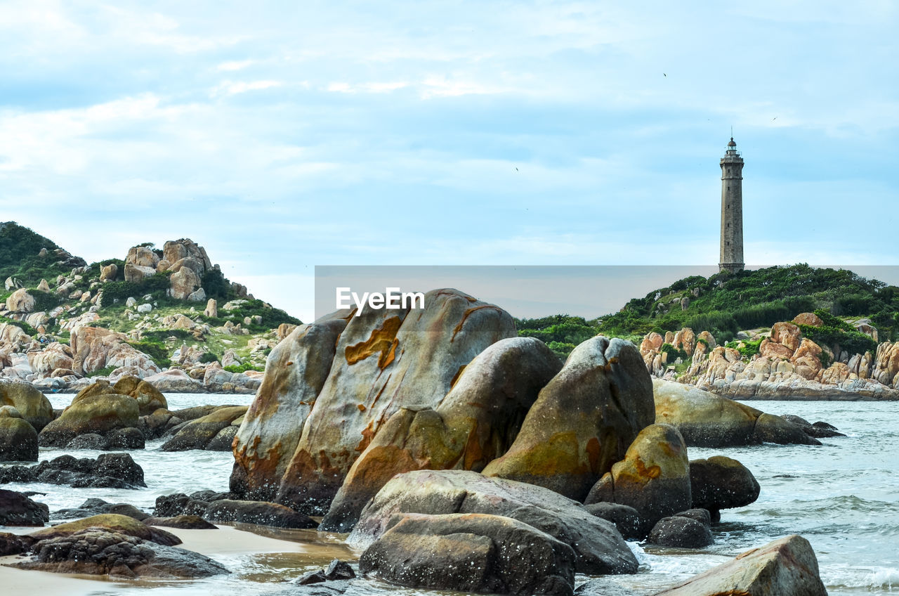 Rocks in sea against cloudy sky