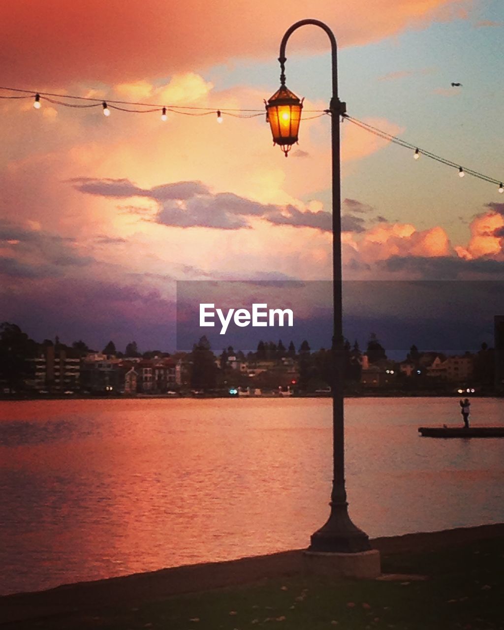 Illuminated street light by river at sunset