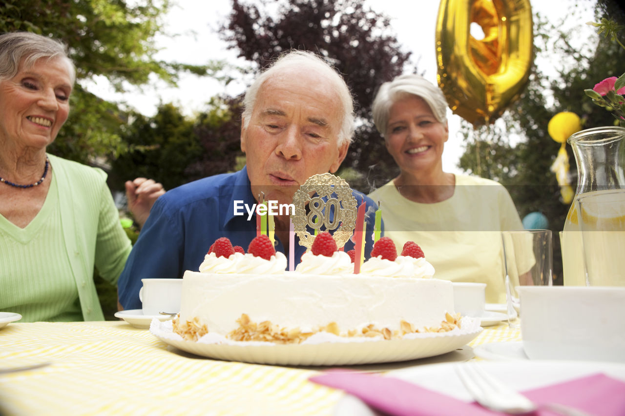 Senior man blowing candle on 80th birthday cake