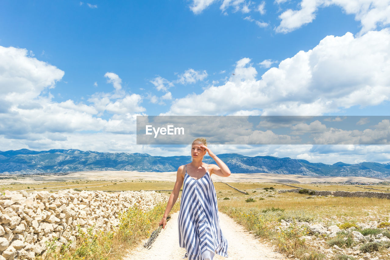 YOUNG WOMAN STANDING ON LAND AGAINST SKY