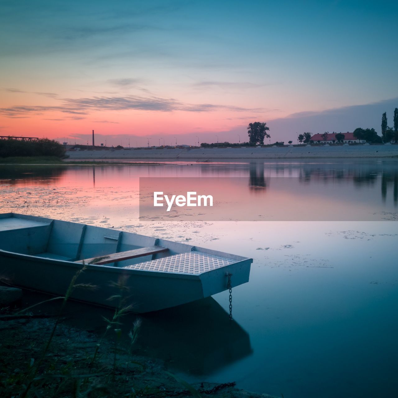 Scenic view of river with moored boat against sky during sunset