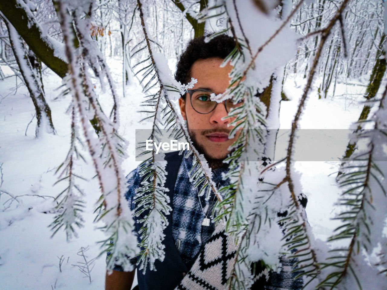 Portrait of man with snow on tree trunk during winter