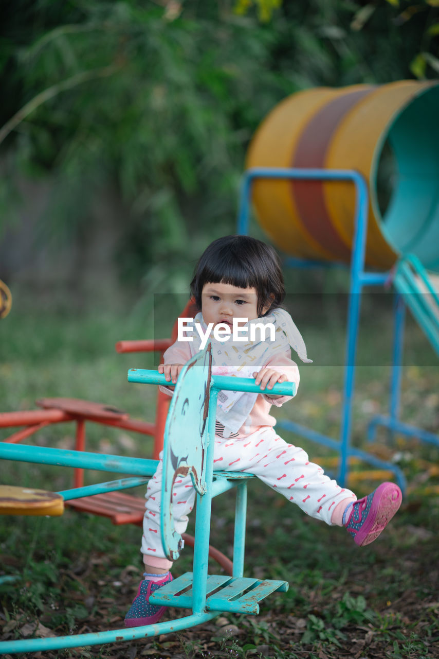 Cute girl looking away while sitting on equipment in playground