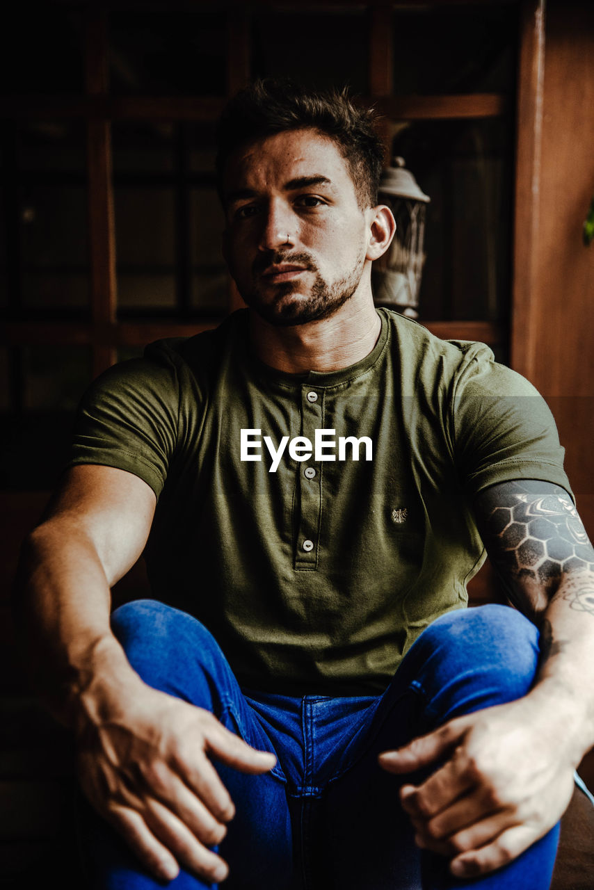 Portrait of young man sitting by plant indoors