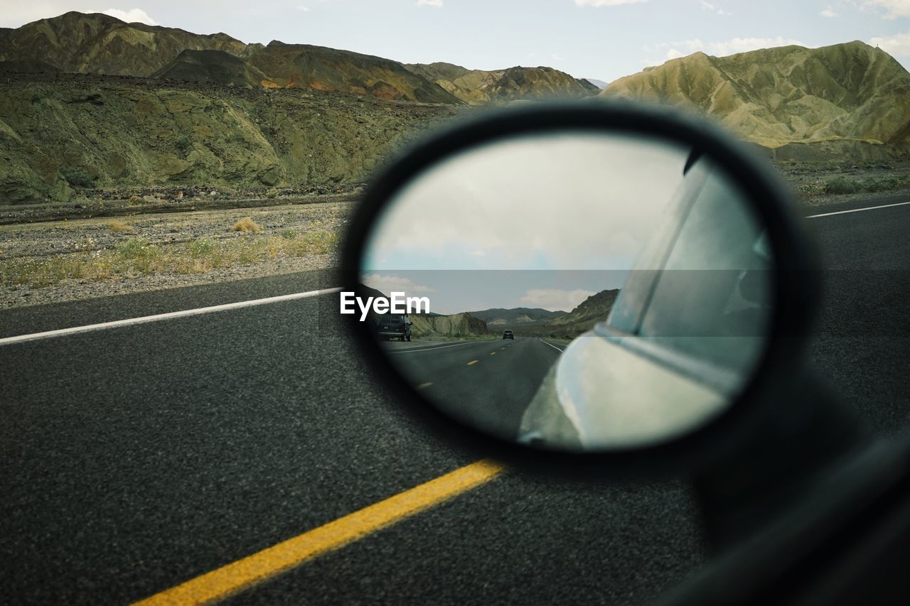 Highway seen from side-view mirror of car against mountains