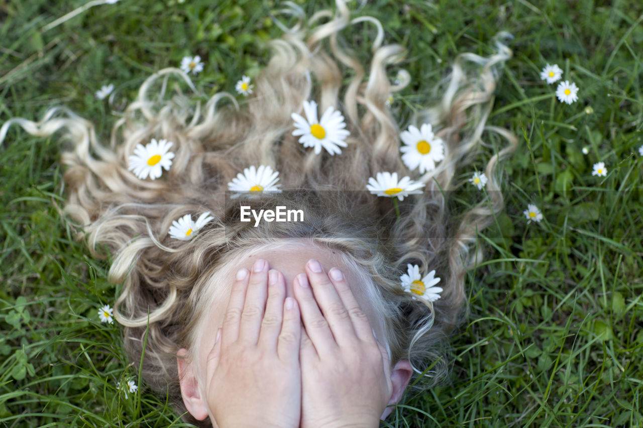 Girl with daisies in her hair covering face