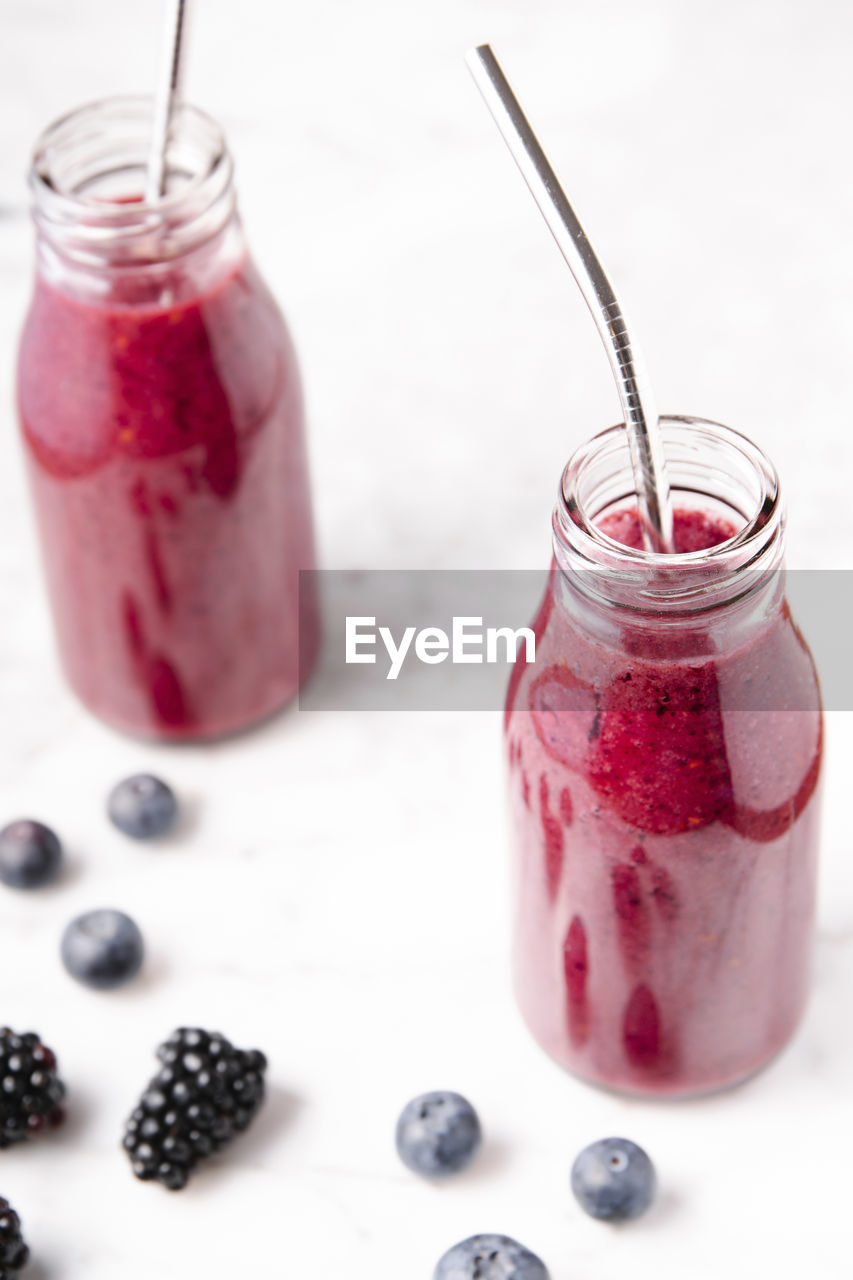 Berry smoothie on glass bottles on a white marble surface. high angle, vertical image.