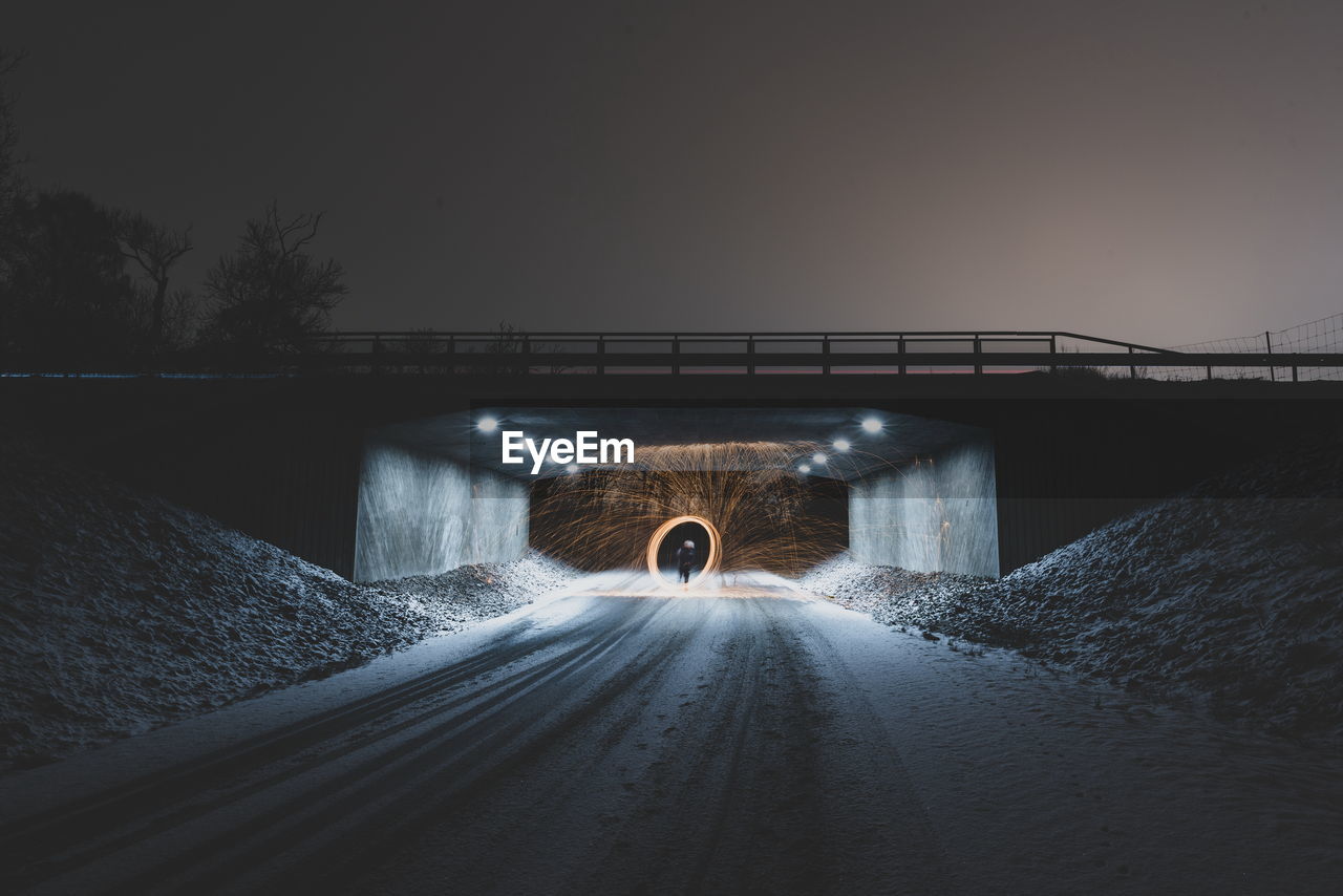 Person spinning wire wool on road under bridge at night