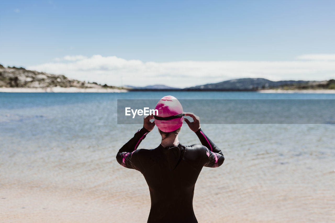 Rear view of woman wearing wetsuit standing at beach