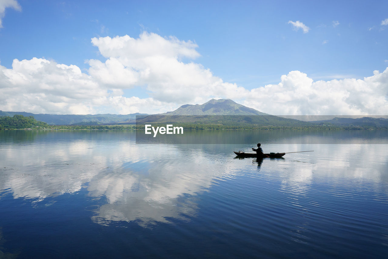 Silhouette man sailing boat on lake against cloudy sky