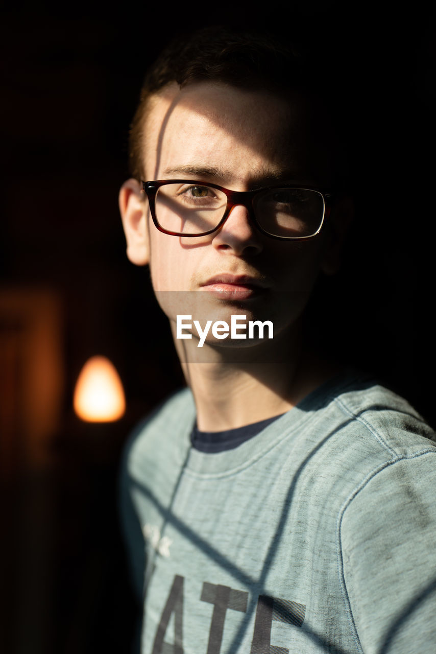 Portrait of young man wearing glasses against black background