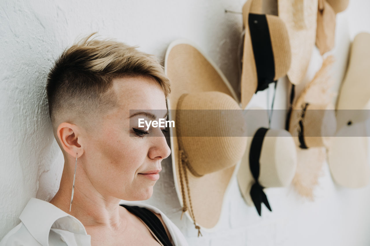 Hipster modern woman and many straw hats like interior decorate the walls in apartment