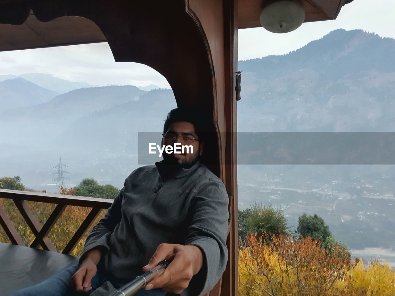 YOUNG MAN USING MOBILE PHONE WHILE SITTING ON MOUNTAINS