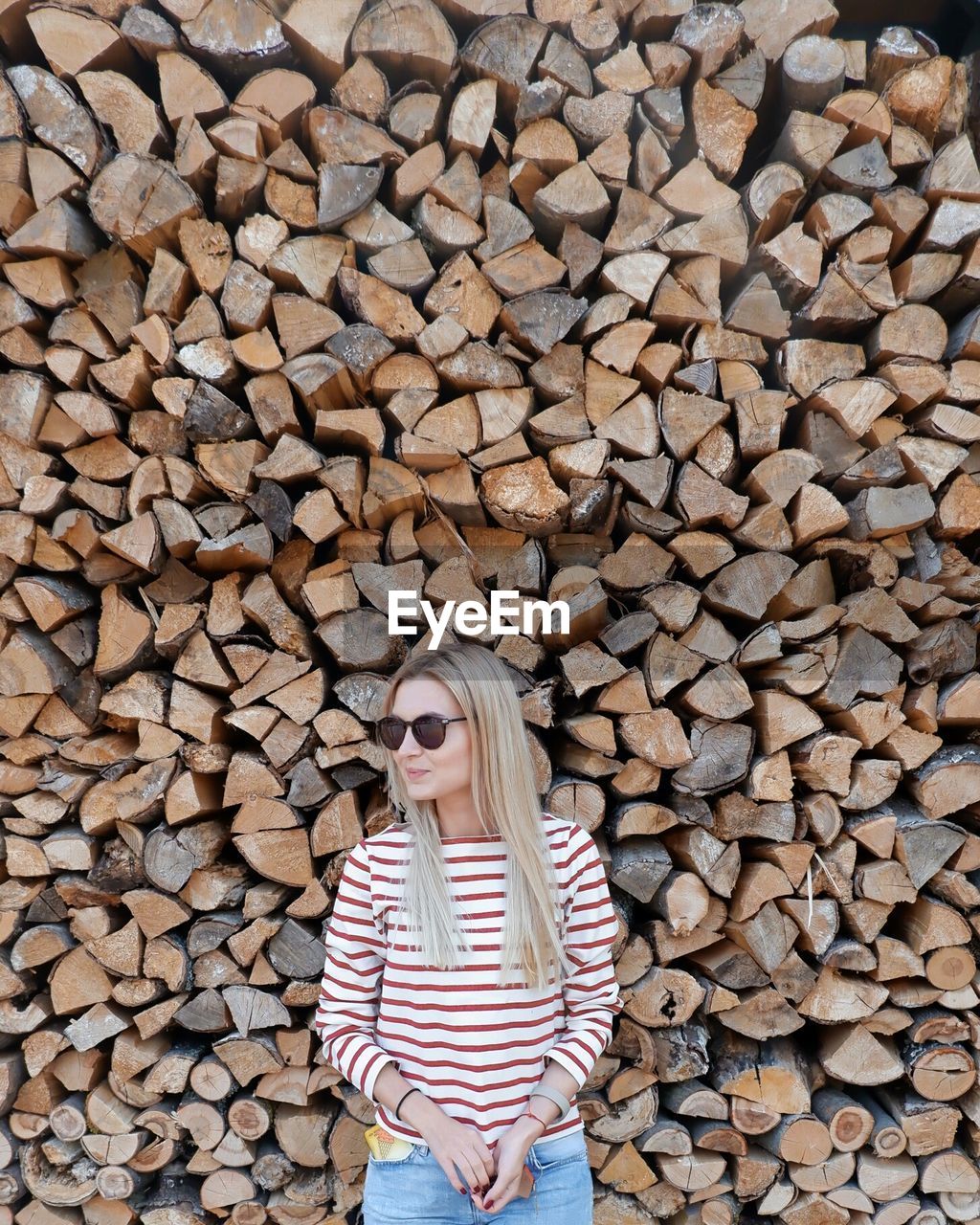 Woman wearing sunglasses standing against woodpile