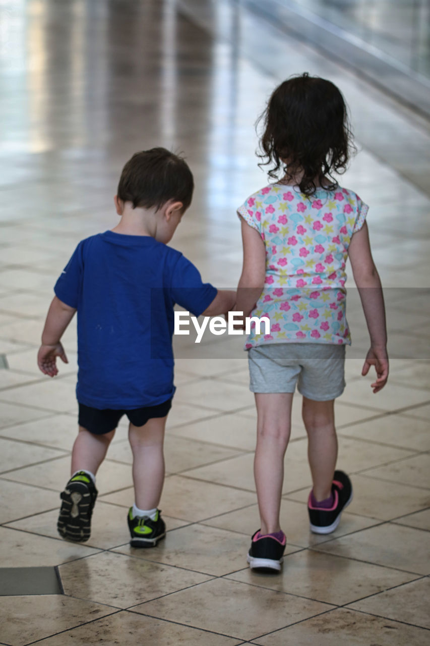 Rear view of cute sibling walking on tiled floor