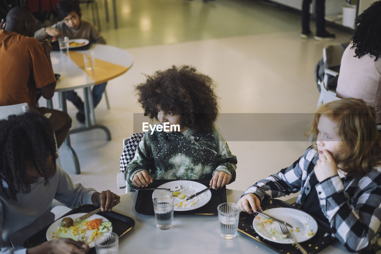 Friends talking to each other sitting at table during lunch break in cafeteria