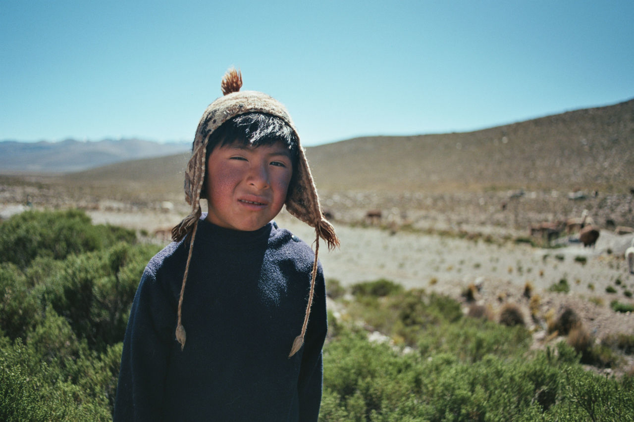 Portrait of boy wearing hat against field and mountain
