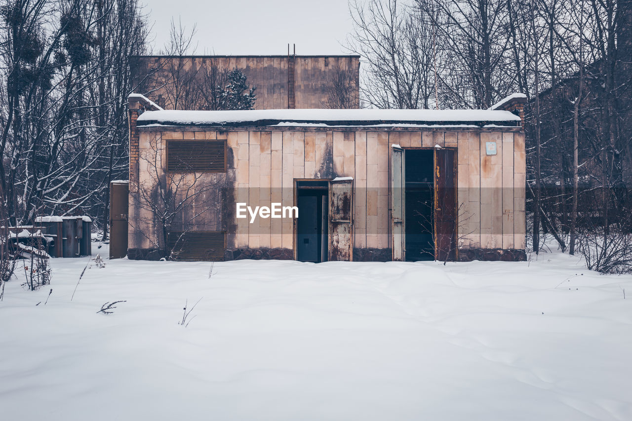 HOUSE AND BARE TREES ON SNOW COVERED FIELD