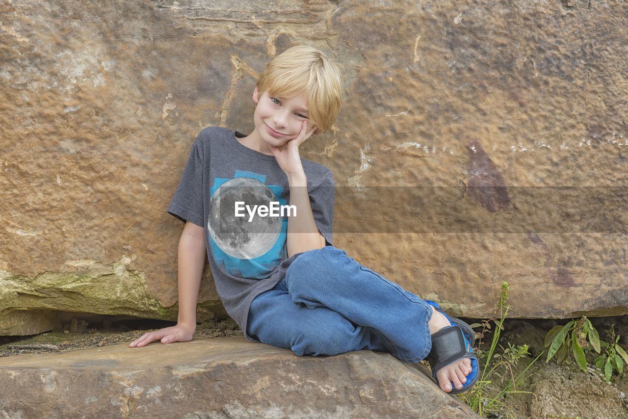 Full length of smiling boy sitting on rock