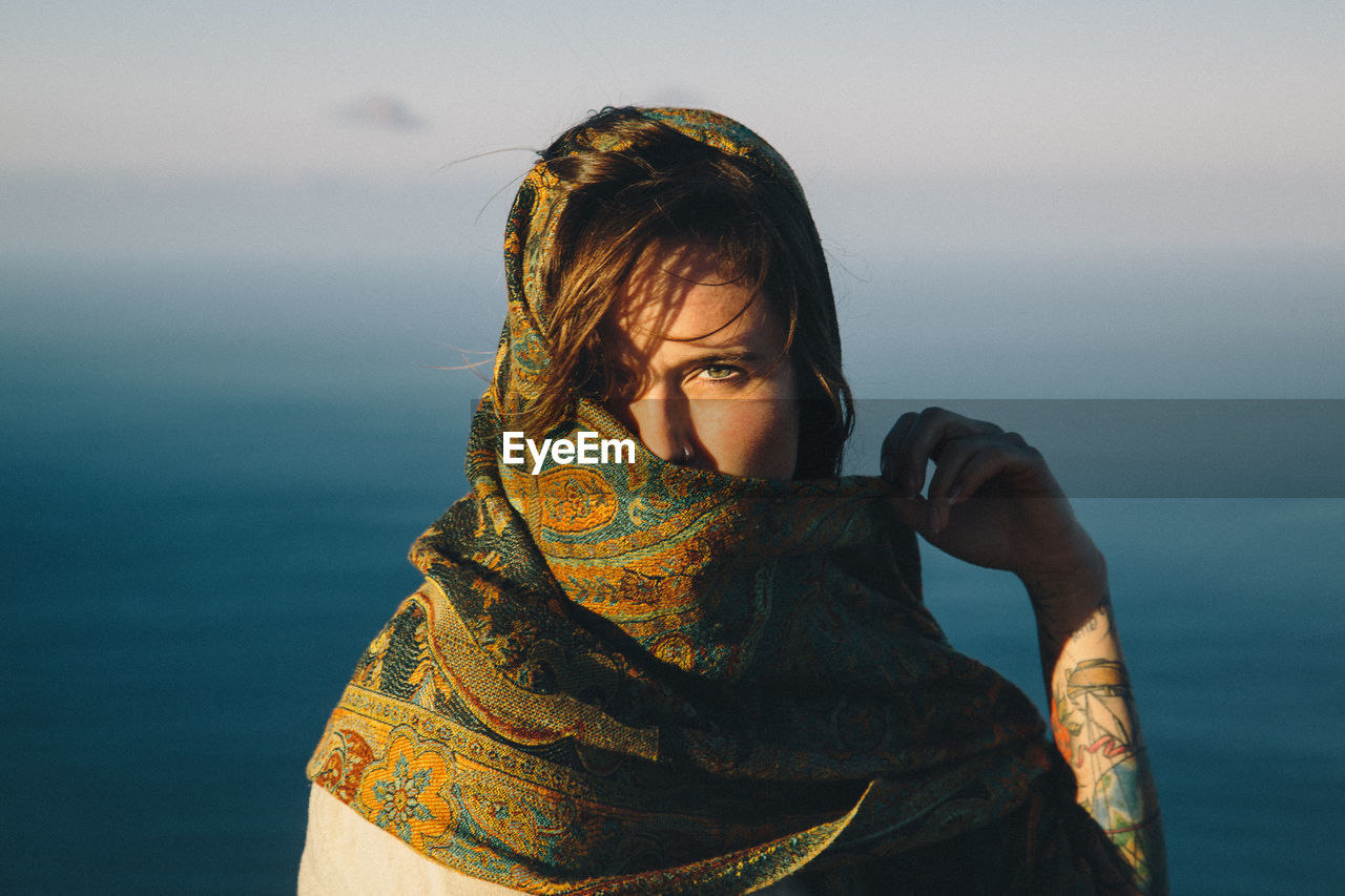 Portrait of young woman covering face with scarf against sea
