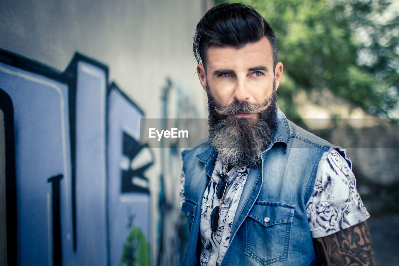 Confident hipster standing by graffiti wall