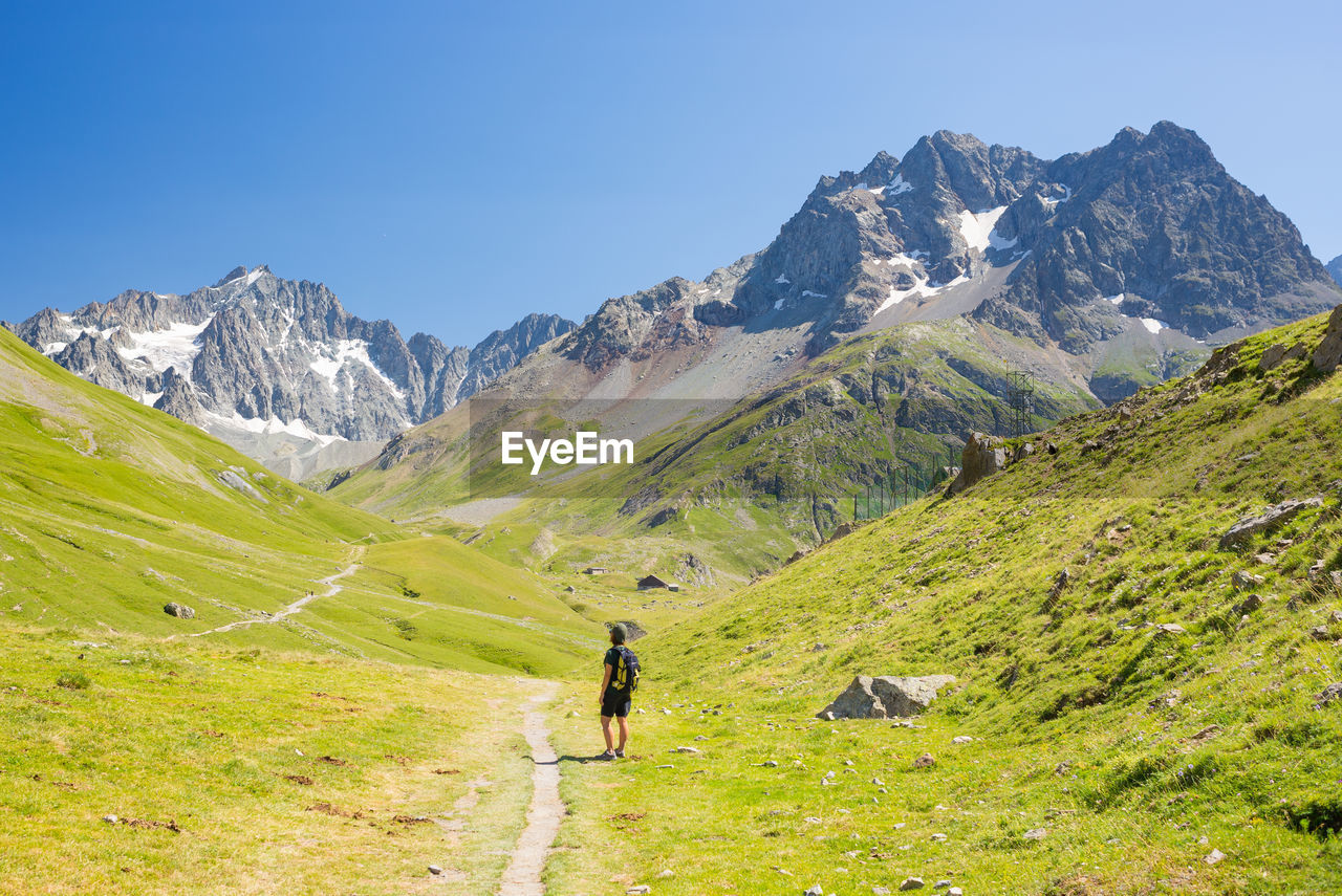 REAR VIEW OF MAN WALKING ON MOUNTAIN