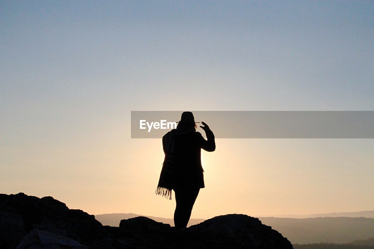 Silhouette woman standing on cliff against clear sky during sunrise