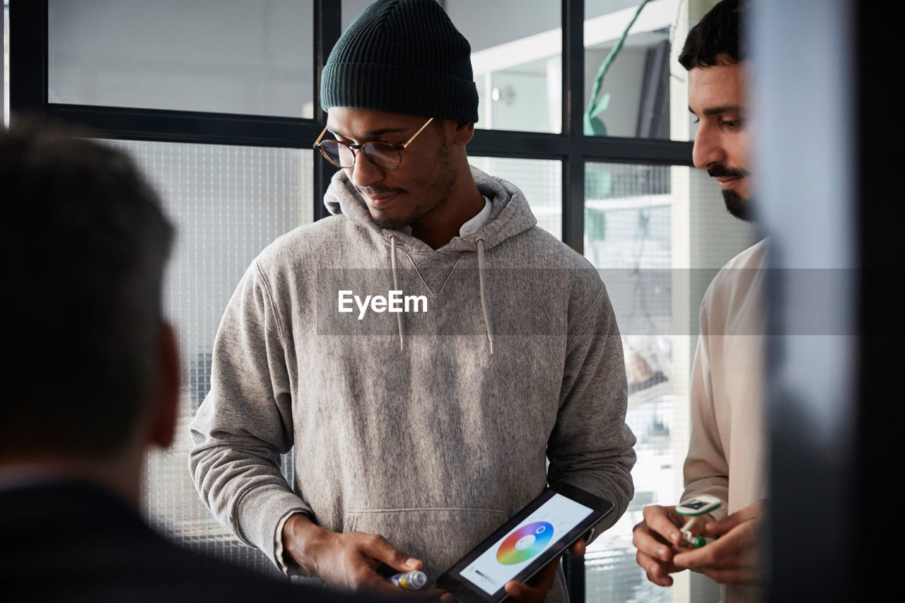 Male entrepreneur holding digital tablet while standing by colleague during meeting in creative office