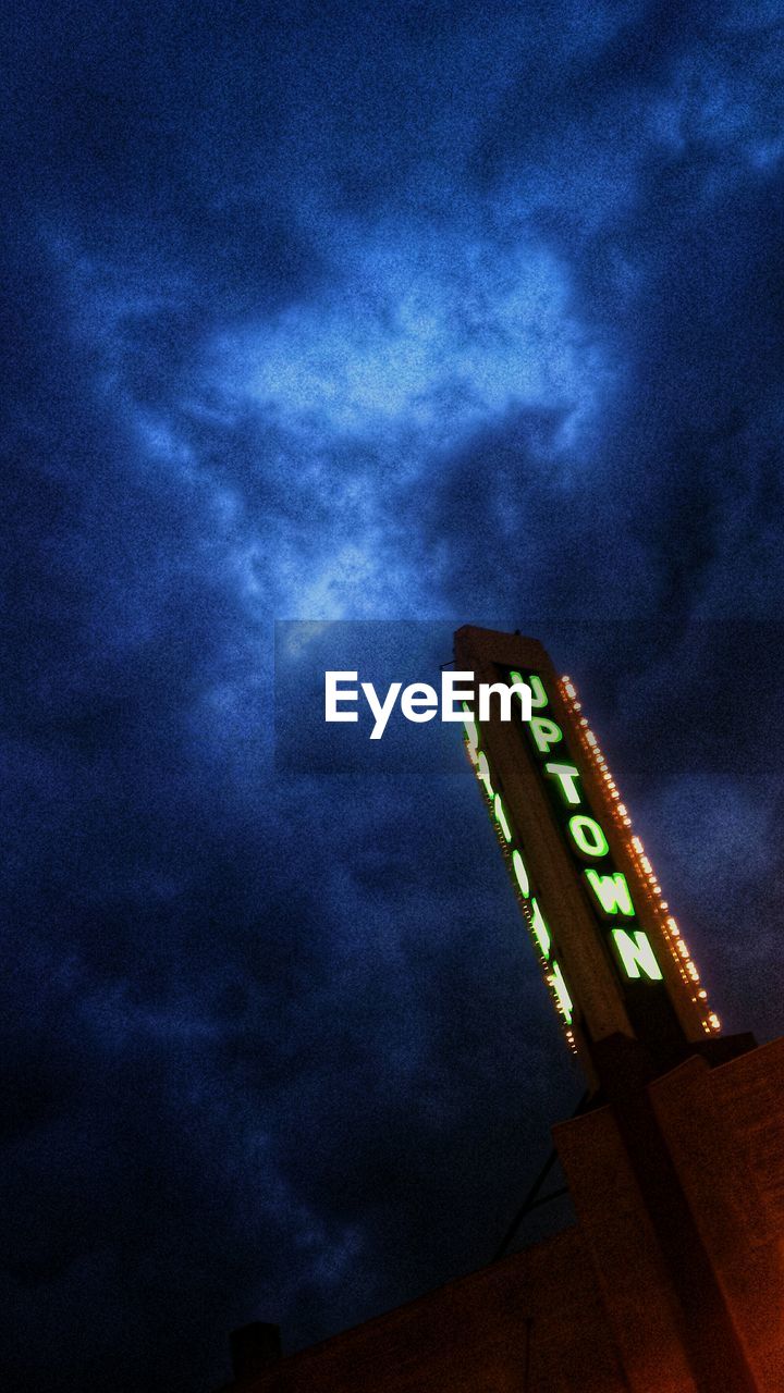 Low angle view of illuminated neon sign against cloudy sky