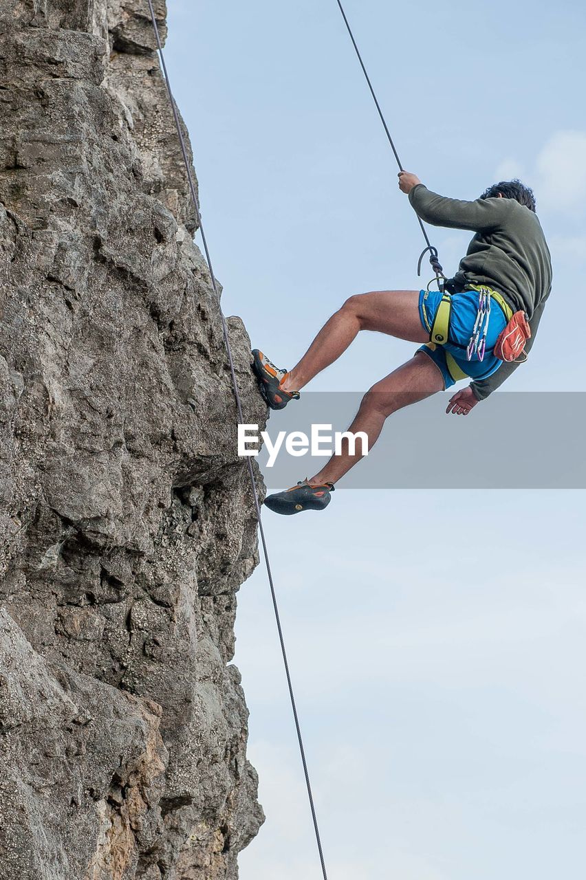 Low angle view of man climbing on rock against sky