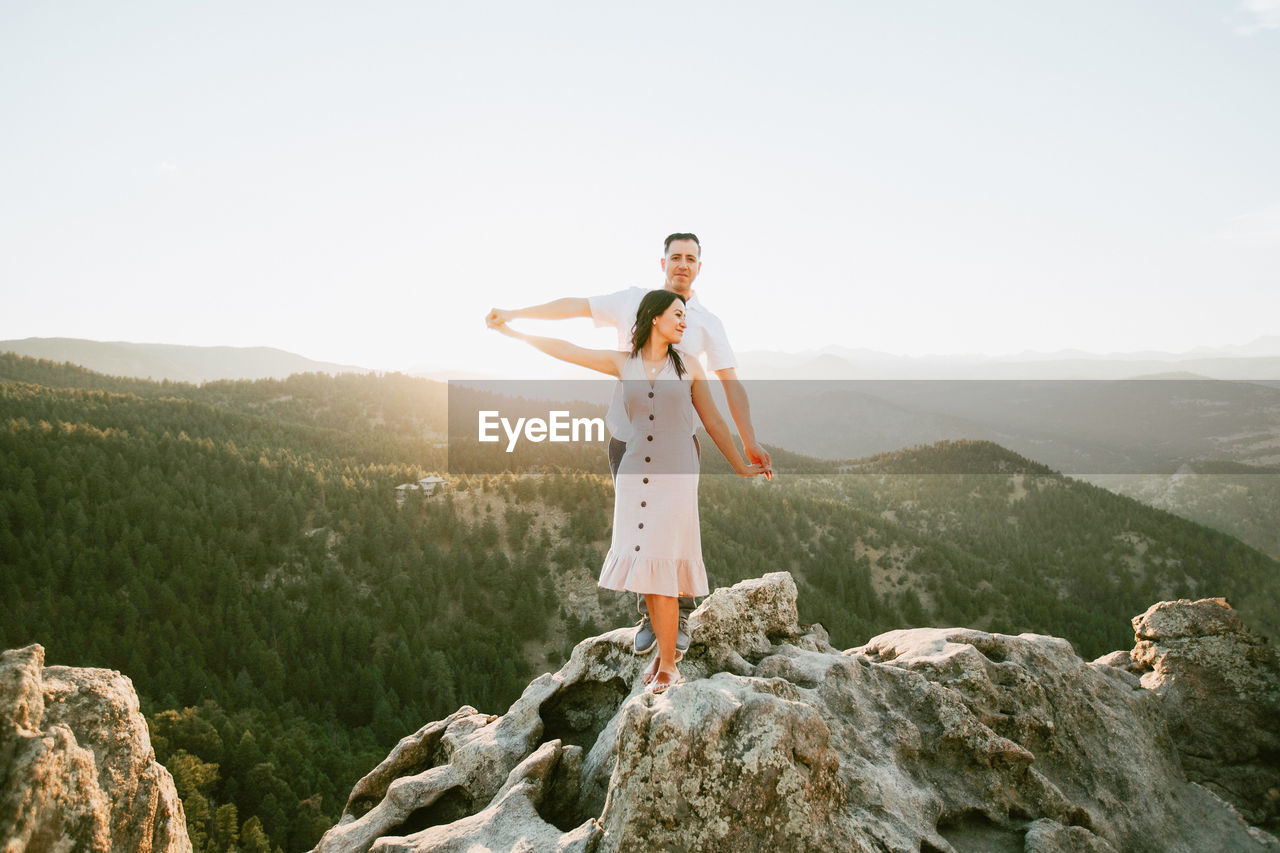 MAN STANDING ON ROCKS AGAINST MOUNTAIN