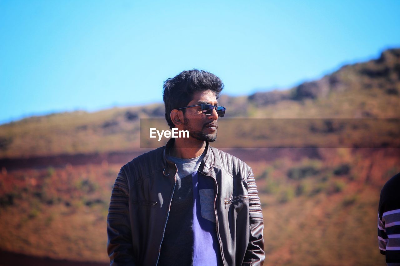 PORTRAIT OF YOUNG MAN STANDING AGAINST SKY